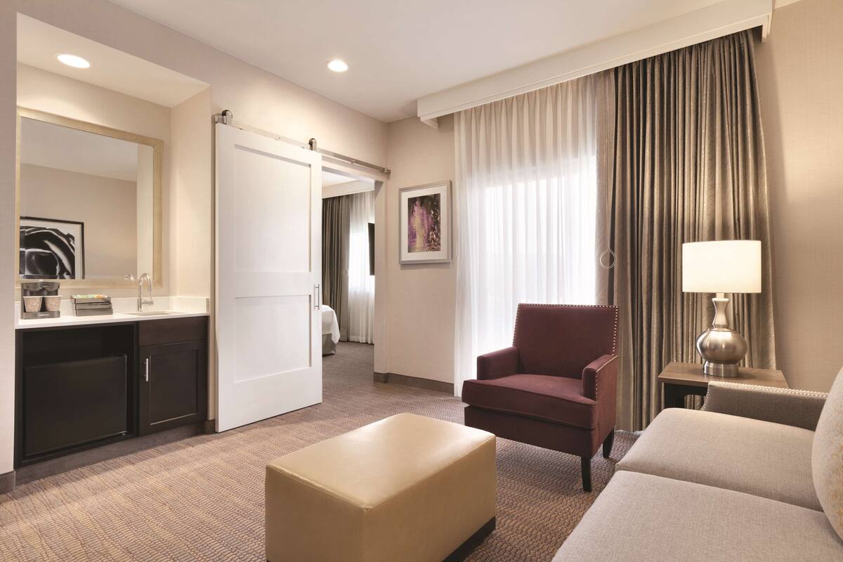 A hotel room with a bed, a desk, a chair, a lamp, and a painting on the wall.
