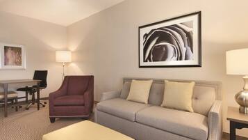 Habitación de hotel con un sofá gris, un sillón rojo, una mesita, un escritorio y un cuadro abstracto enmarcado en la pared.