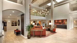 A spacious lobby with a high ceiling, a central seating area with a sofa and chairs, a large chandelier, and a staircase leading to an upper level. - Embassy Suites by Hilton Temecula Valley Wine Country (Temecula)