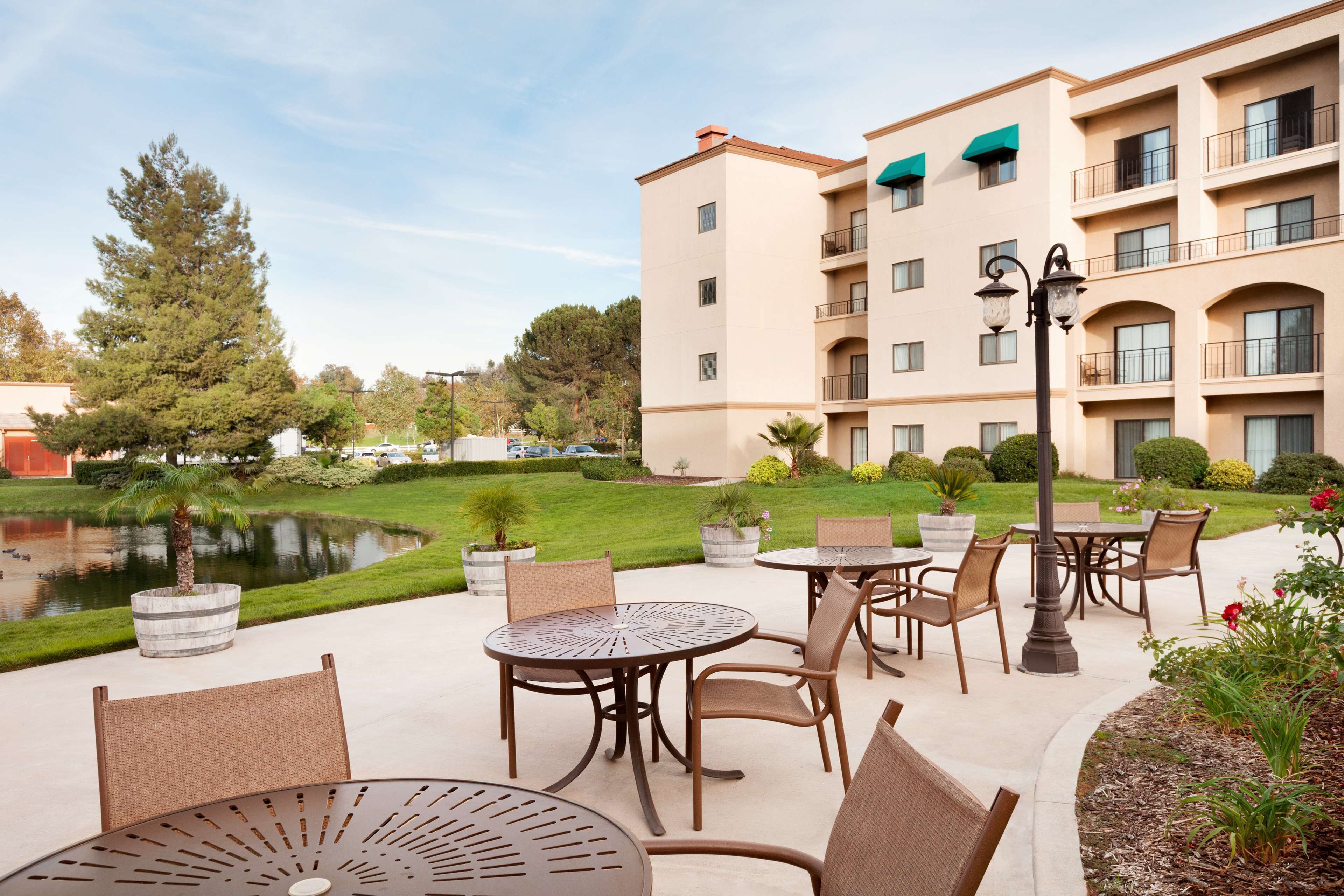 Un espace extérieur aménagé en terrasse, avec des tables et des chaises rondes, un bassin et un bâtiment doté de plusieurs balcons.
