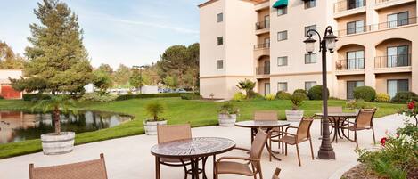 Un espace extérieur aménagé en terrasse, avec des tables et des chaises rondes, un bassin et un bâtiment doté de plusieurs balcons.