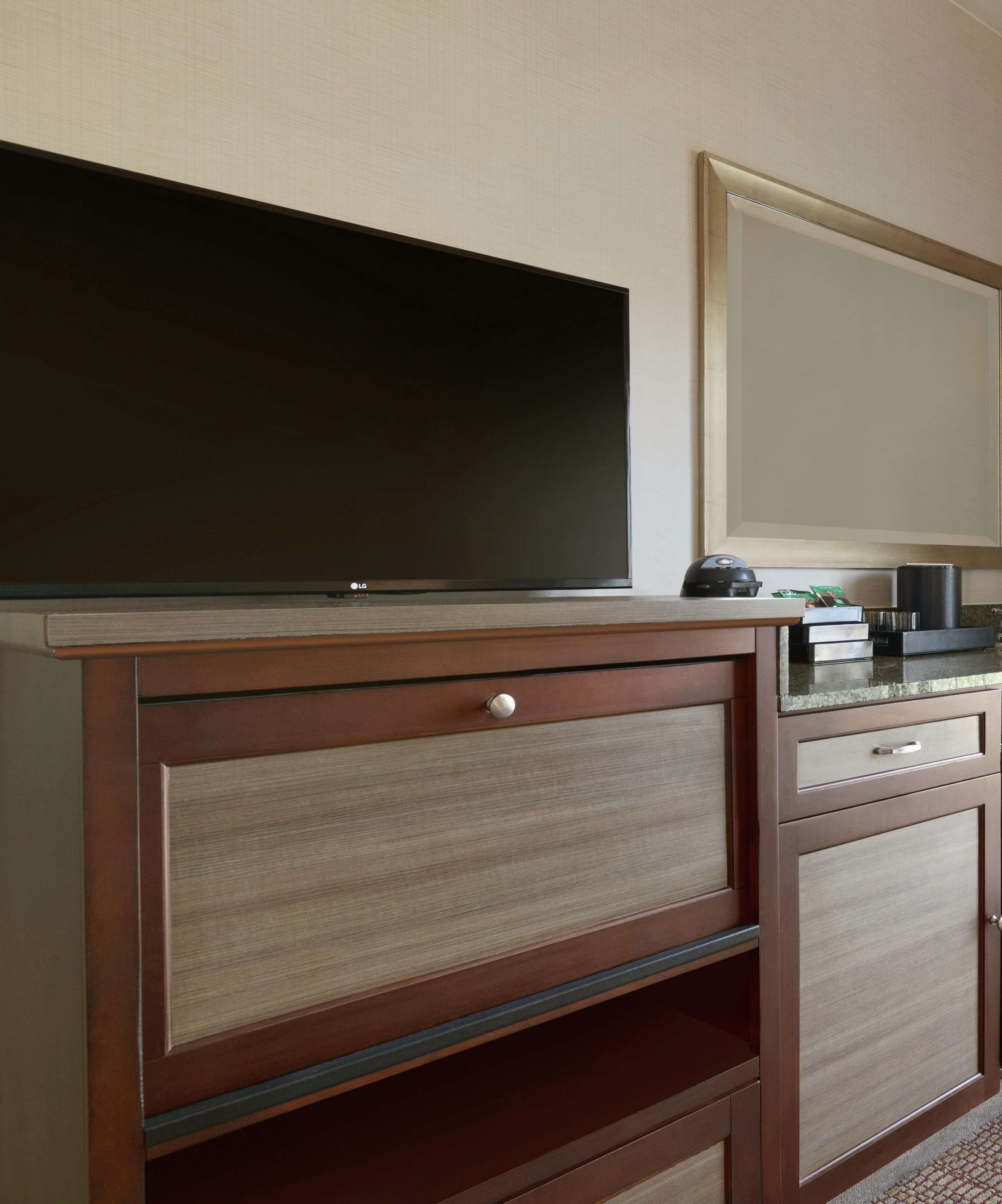 A wooden TV stand with a flat-screen TV, a coffee maker, and a framed mirror.