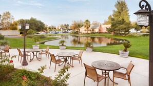 An outdoor patio area with round tables and chairs, a pond, and a view of a residential neighborhood. - Embassy Suites by Hilton Temecula Valley Wine Country (Temecula)