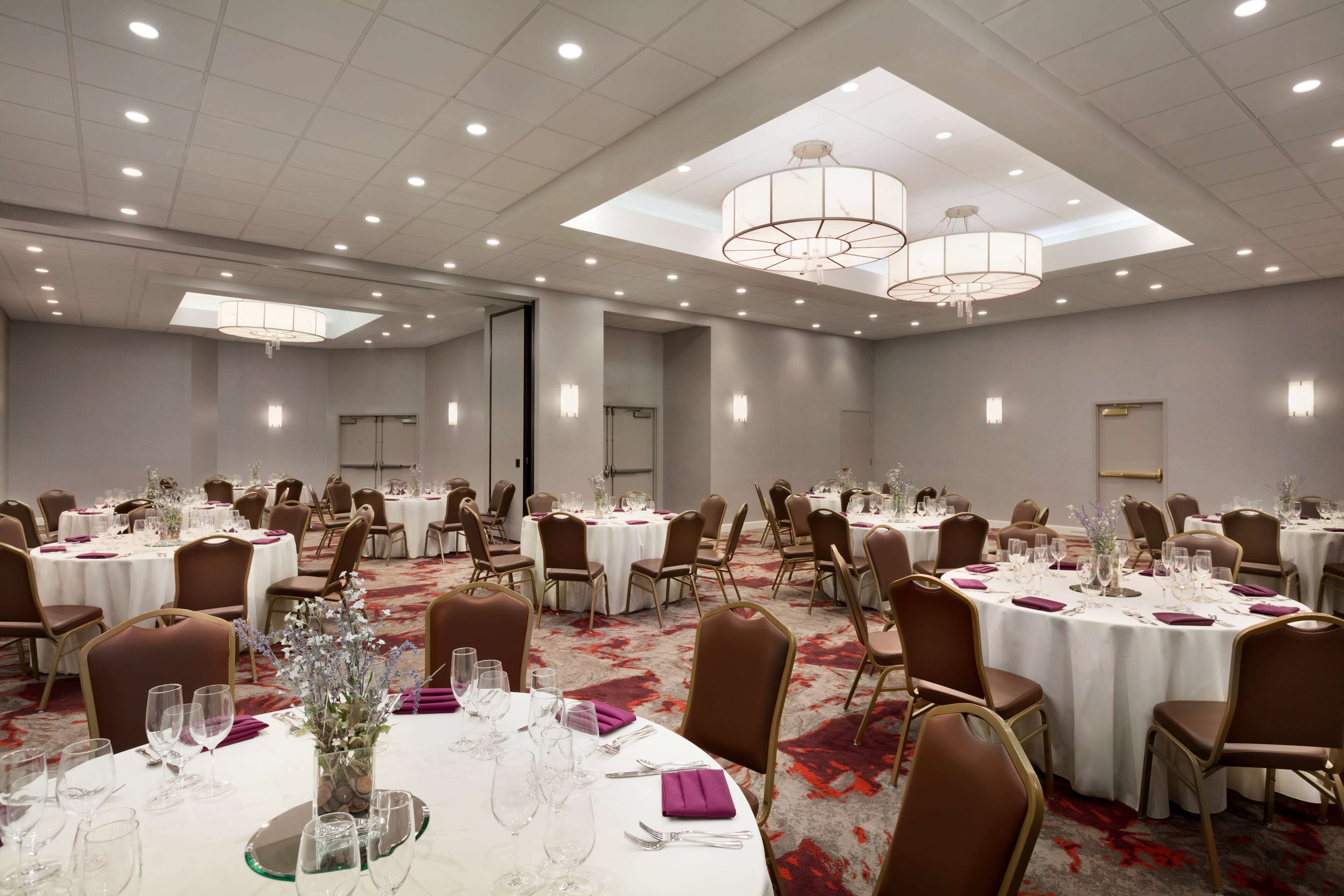A banquet hall with round tables, brown chairs, and white tablecloths.