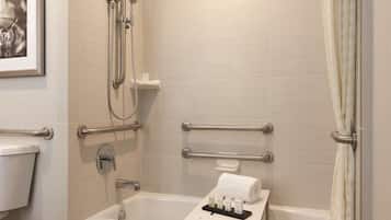 A bathroom with a bathtub, shower, and toilet. There are handrails and a towel rack.
