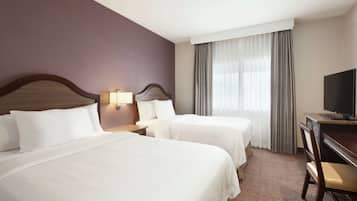 Une chambre d’hôtel avec deux lits, un bureau, une chaise, une télévision et une fenêtre avec des rideaux.