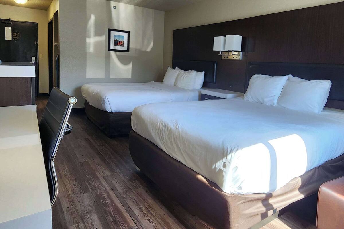 A hotel room with two beds, a desk, and a chair.