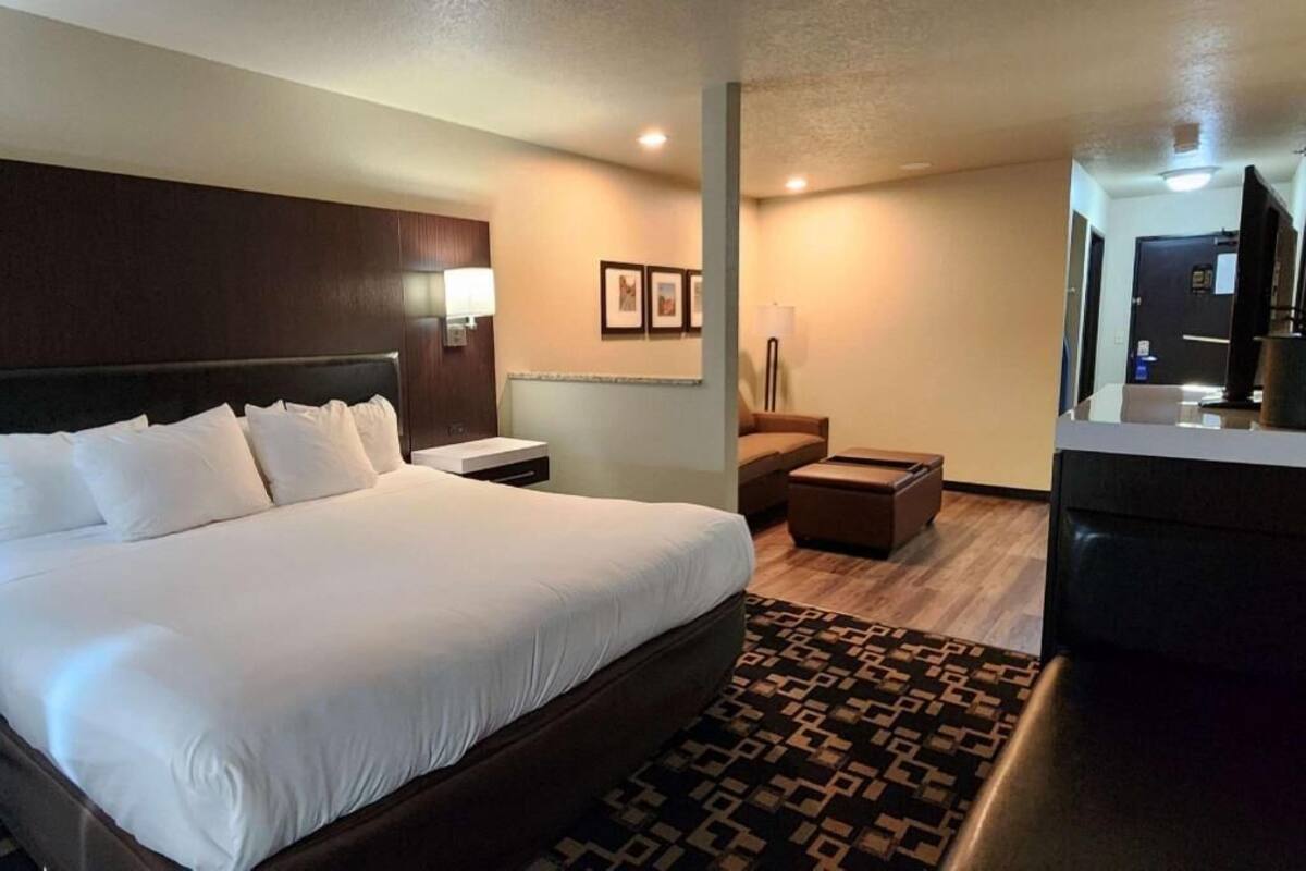 A hotel room with a large bed, a desk, a chair, a TV, and a small table.