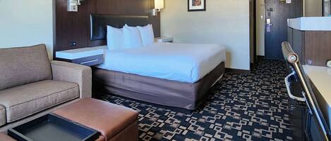 A hotel room with a bed, a sofa, a desk, and a patterned carpet.