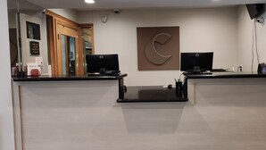 Uma mesa de recepção com dois monitores de computador, uma câmera de segurança e uma grande placa fixada na parede.