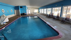 Uma piscina interior ampla com pistas demarcadas, espreguiçadeiras ao longo da borda e vista para o estacionamento através de grandes janelas.