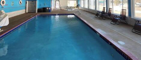 Una piscina con borde de azulejos, un vestuario con ducha y sillones de descanso junto a las ventanas.