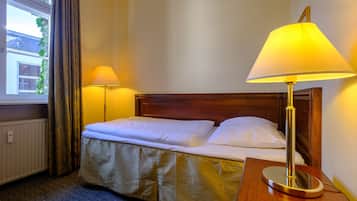 A hotel room with a bed, two bedside lamps, a wooden headboard, and a window with curtains.