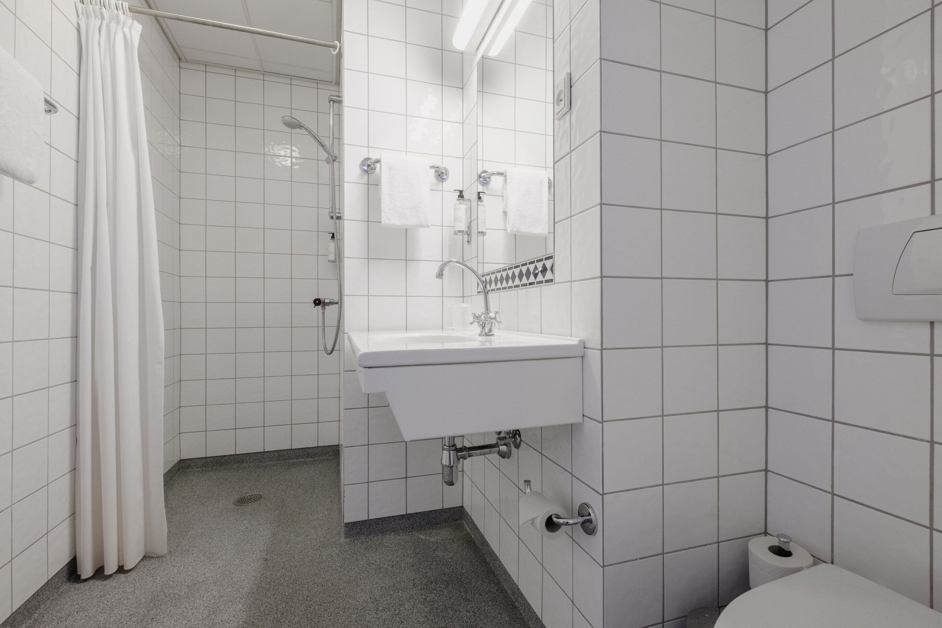Un baño con azulejos blancos, lavamanos, ducha e inodoro.