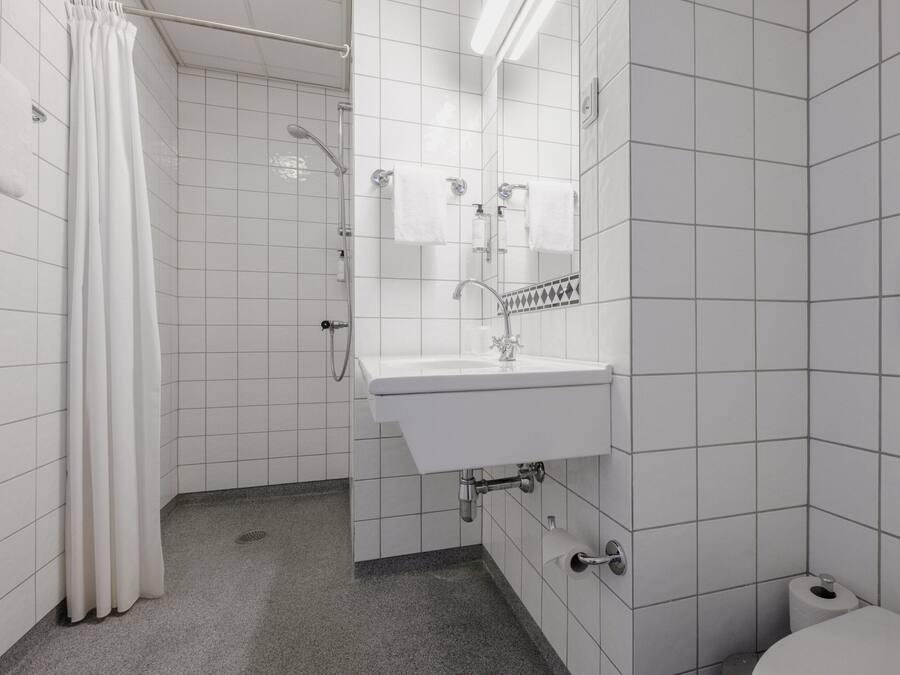 Un baño con azulejos blancos, lavamanos, ducha e inodoro.