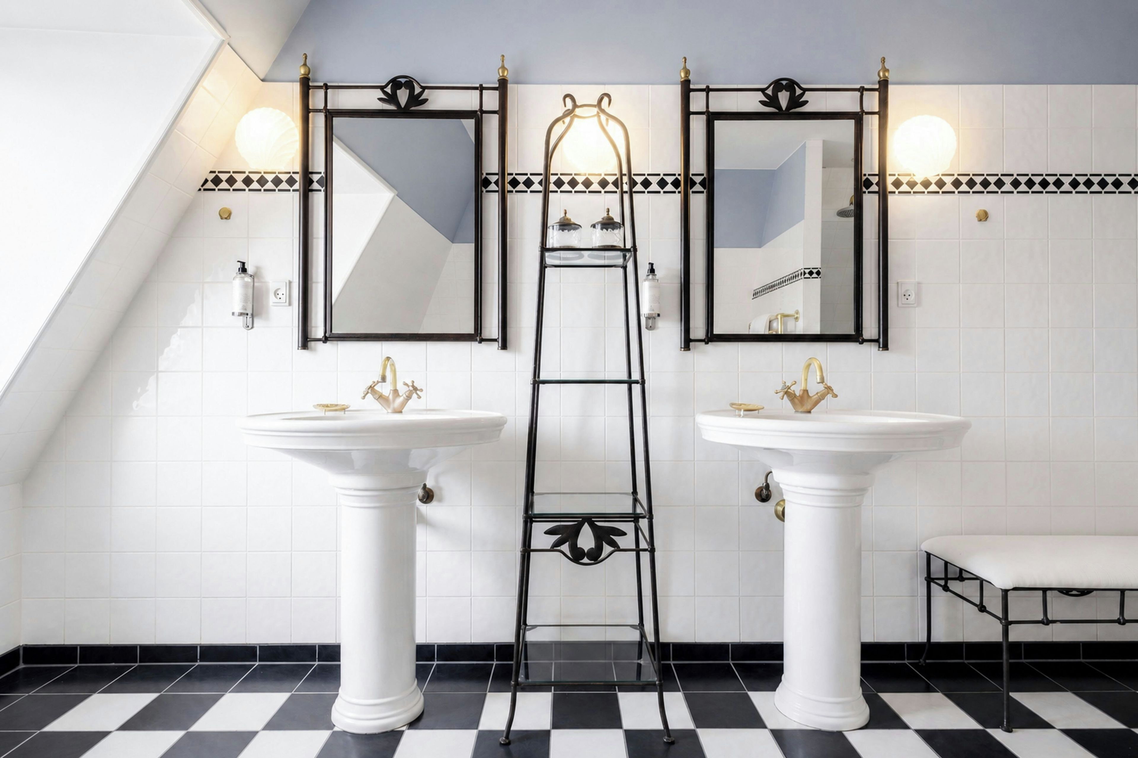 Une salle de bain avec deux lavabos blancs sur pied, une échelle en métal noir et un banc.