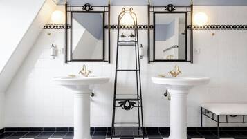 Une salle de bain avec deux lavabos blancs sur pied, une échelle en métal noir et un banc.