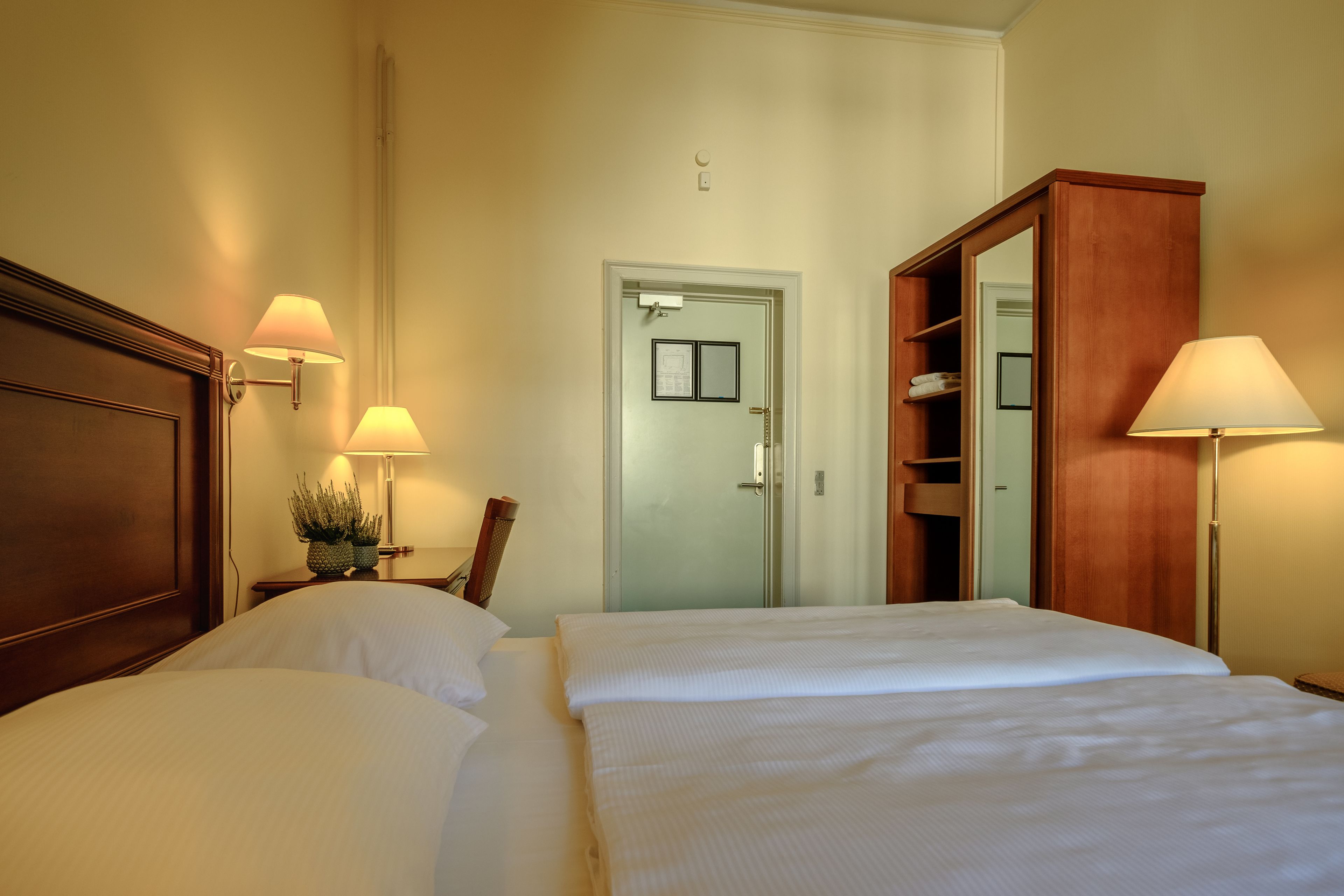 Een hotelkamer met twee bedden, een houten garderobe, een spiegel en twee wandlampen.