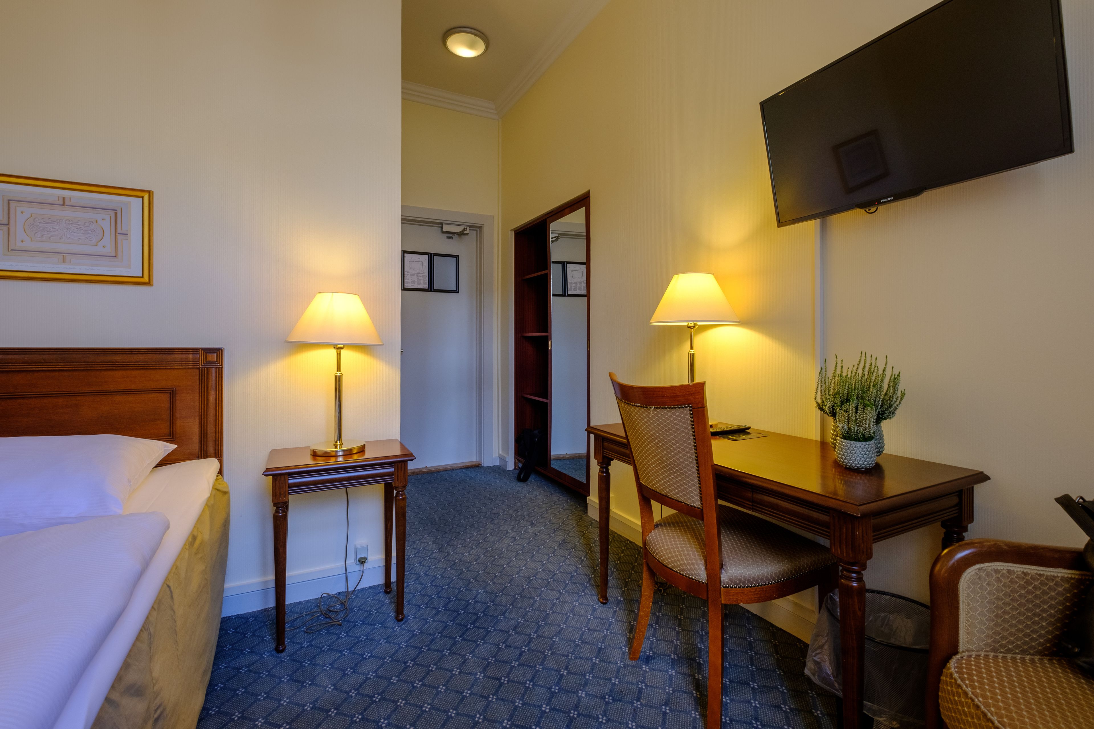 A hotel room with a bed, a desk with a chair, a television, and a mirror.