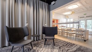 A modern hotel lobby with two dark chairs, a patterned carpet, and a view into a dining area with light-colored chairs and a counter. - Four Points Flex by Sheraton Roskilde (Roskilde)