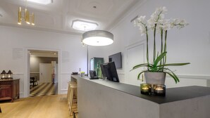 A modern hotel lobby with a reception desk, wooden flooring, a checkered floor pattern, a large pendant light, and a potted orchid plant. - Four Points Flex by Sheraton Roskilde (Roskilde)