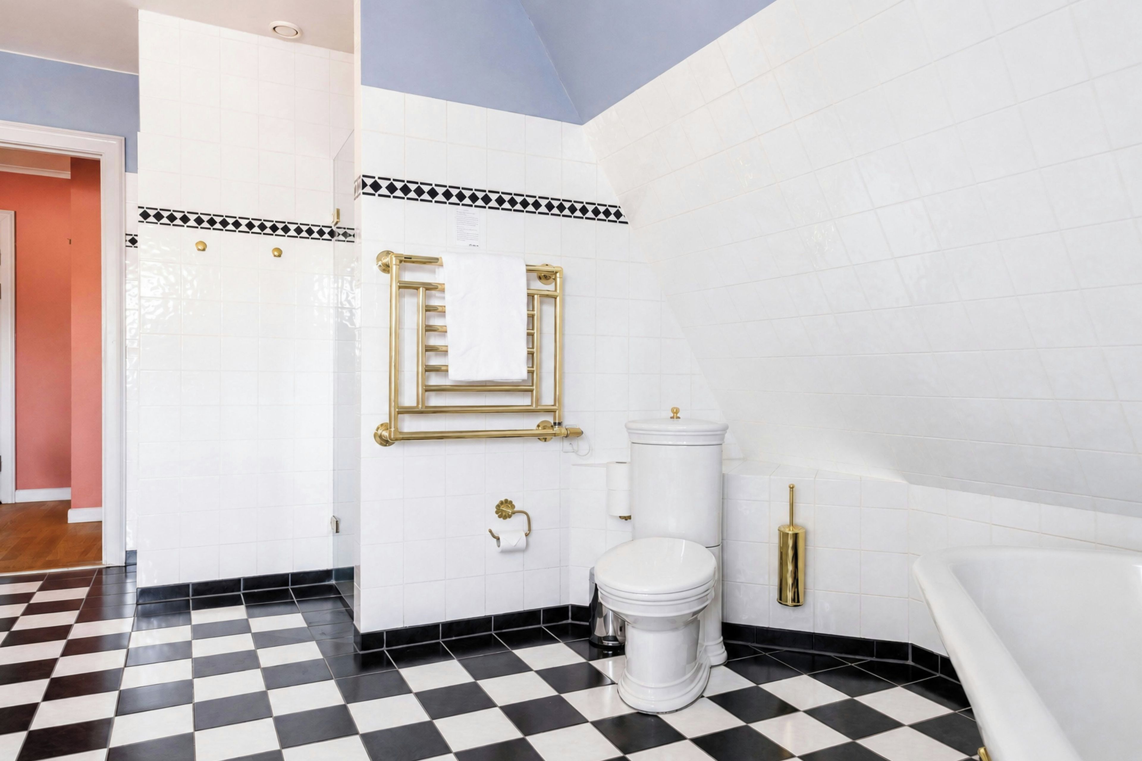 Une salle de bain avec un carrelage à motifs, des murs blancs, des toilettes blanches et un porte-serviettes doré.