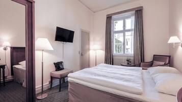 A hotel room with a large bed, two bedside lamps, a flat-screen TV, a window with curtains, a chair, and a small table with a lamp.