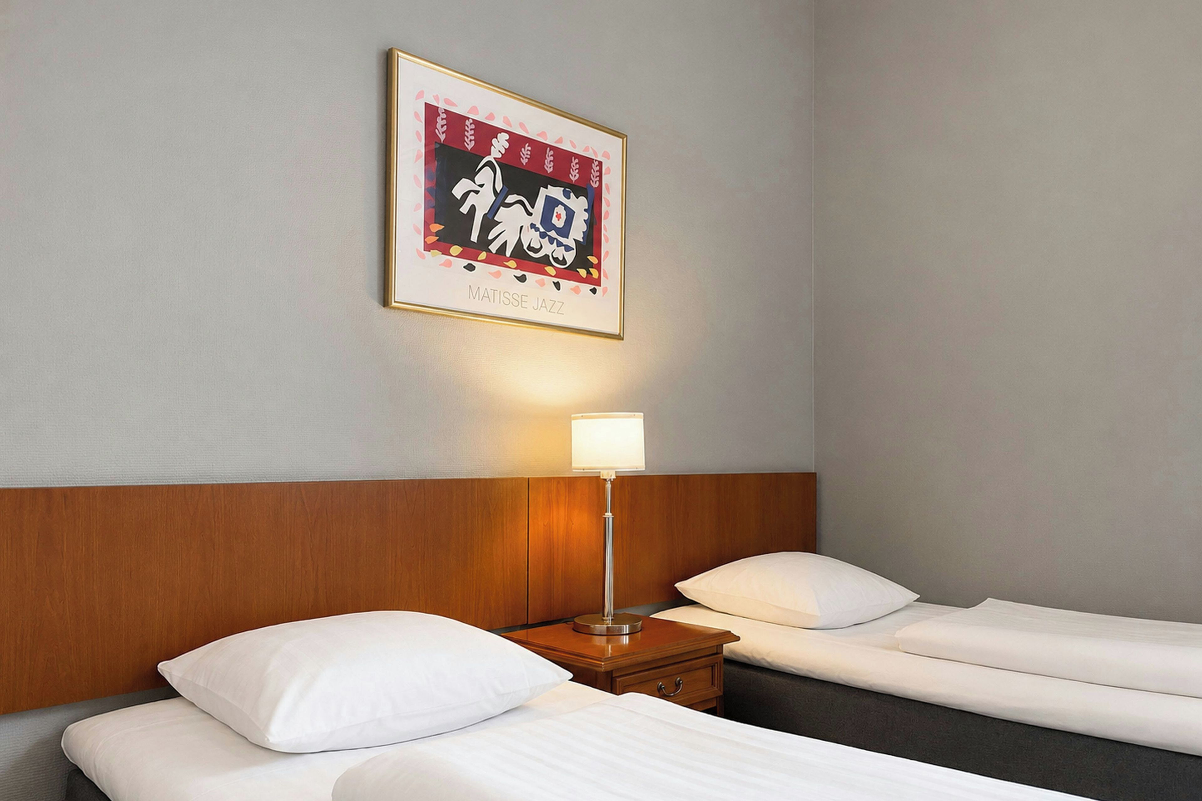 Habitación de hotel con dos camas, una mesita de noche, una lámpara y una obra de arte enmarcada en la pared.
