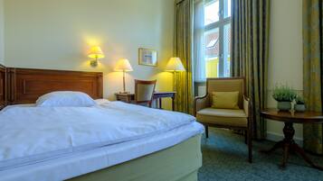 A hotel room with a large bed, two bedside lamps, a chair, a small table with plants, and a window with curtains.