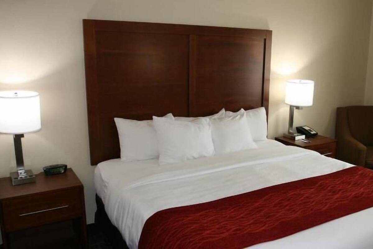 A hotel room with a large bed, two bedside tables, a chair, and a lamp on each side of the bed.
