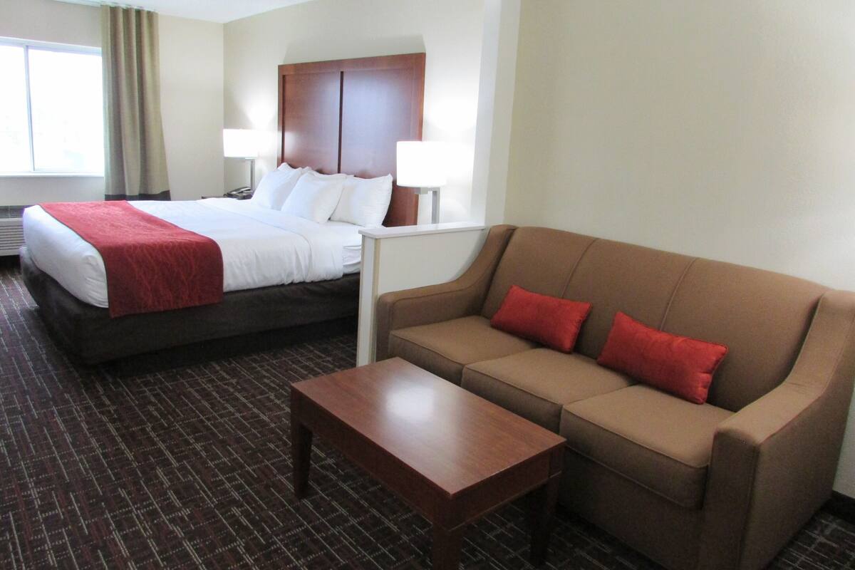 A hotel room with a bed, a sofa, a coffee table, and a nightstand with lamps.