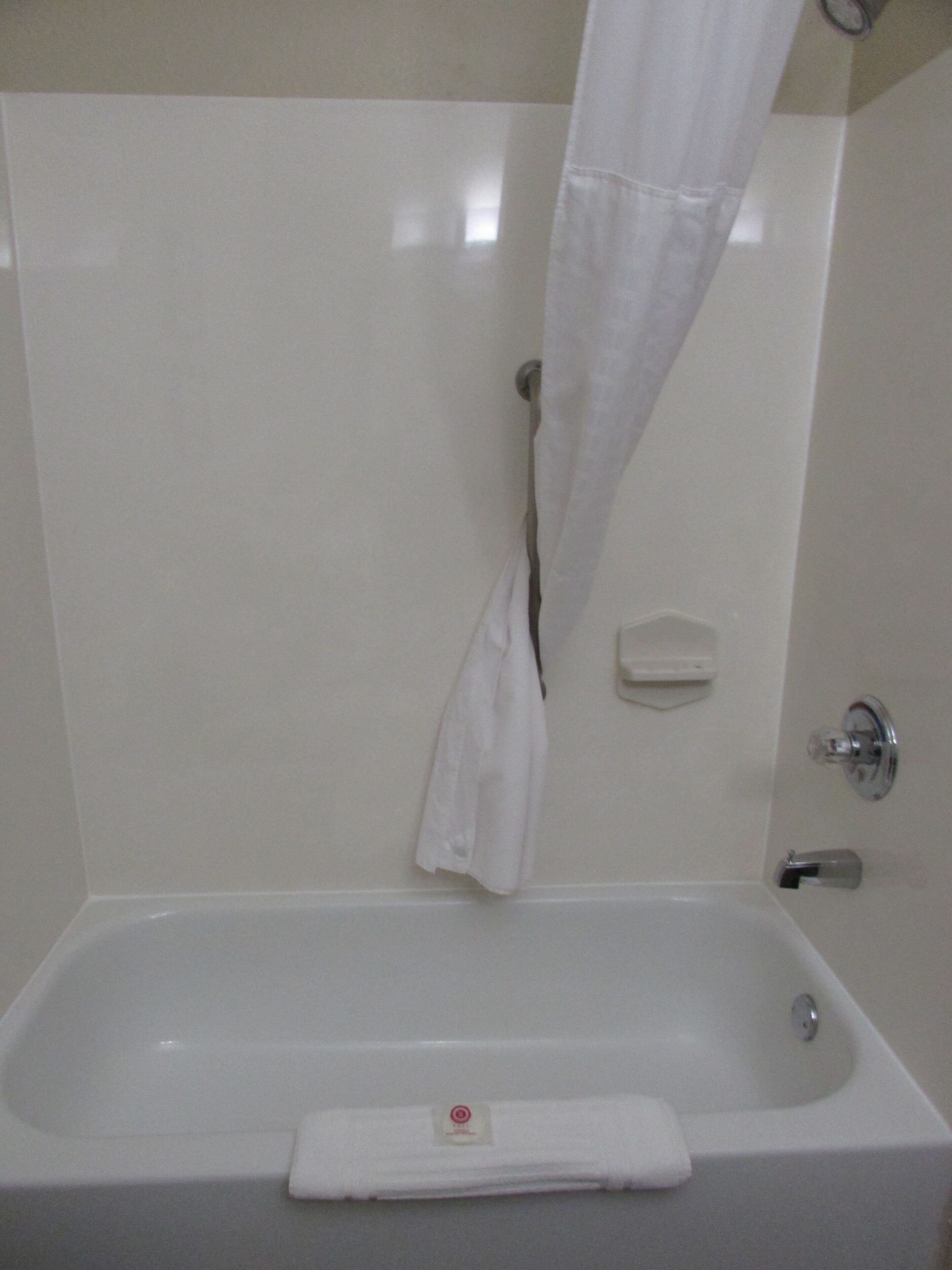 Una bañera blanca con una toalla en el borde, un jabonera y una barra para cortina de ducha.