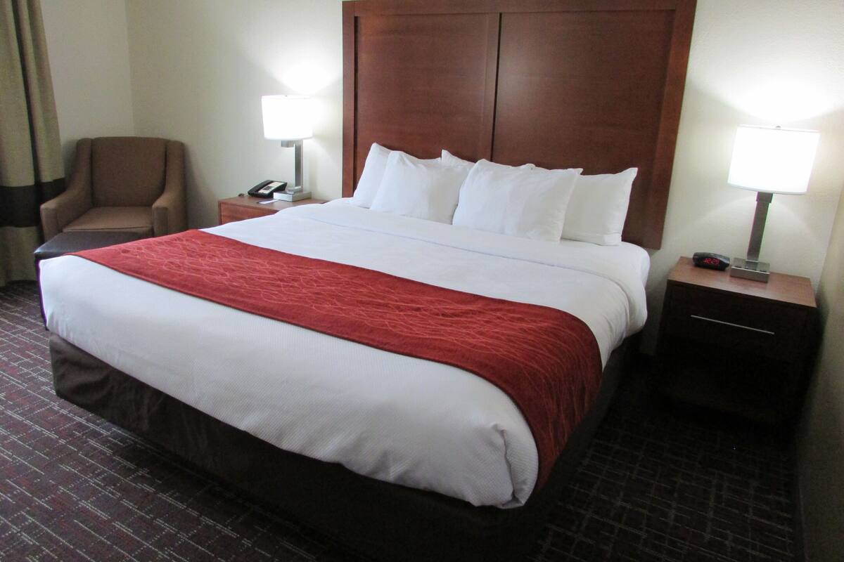 A hotel room with a large bed, two bedside tables, a chair, and a lamp.