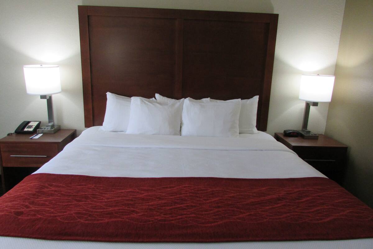 A neatly made bed with white linens and a red blanket, flanked by two bedside tables with lamps and a phone.