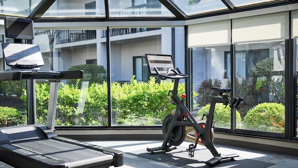 A modern gym with a treadmill, stationary bike, and exercise mat, featuring large windows and a view of greenery. - Courtyard by Marriott Kansas City Overland Park/Metcalf (Overland Park)