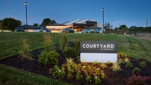 A Courtyard by Marriott hotel with a well-maintained lawn, a signboard, and several parked cars. - Courtyard by Marriott Kansas City Overland Park/Metcalf (Overland Park)