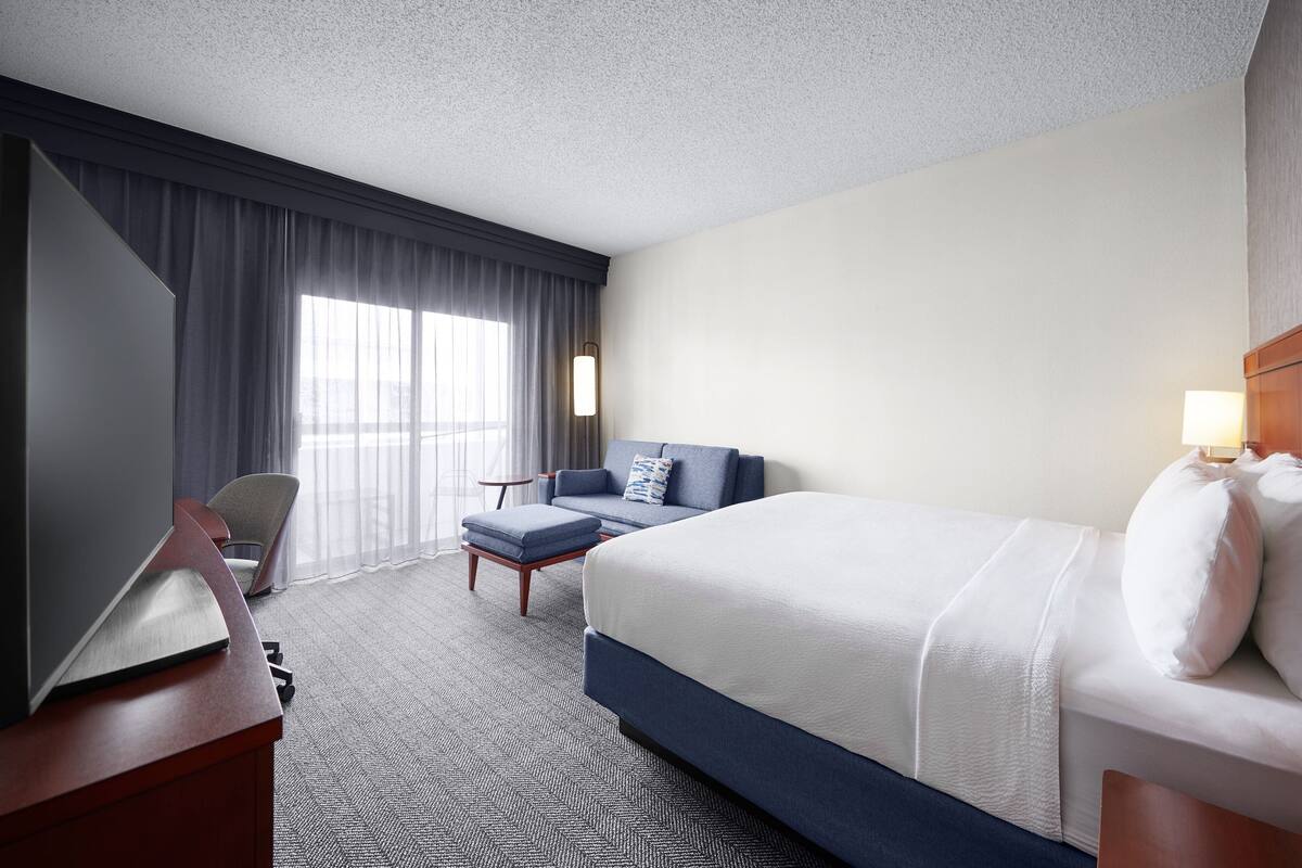 Ein Hotelzimmer mit einem großen Bett, einem Schreibtisch mit Stuhl, einer Couch und einem Fernseher.