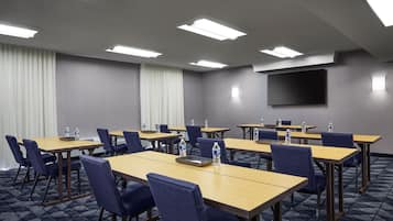 A conference room with multiple tables and chairs, equipped with water bottles, a flat-screen TV, and a projector.