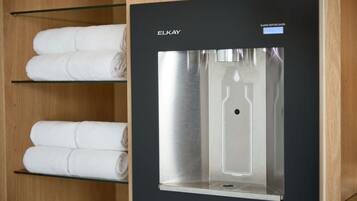 A modern water dispenser with a stainless steel finish, labeled 'ELKAY', and a shelf with neatly folded white towels.