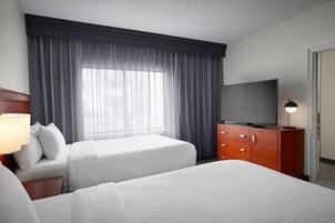 A hotel room with two beds, a TV, a dresser, and a window with curtains.