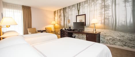 Habitación de hotel con dos camas, un escritorio, un televisor y un mural temático de bosque.