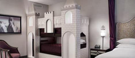 Une chambre d’hôtel avec un lit superposé décoré sur le thème d’un château, un tableau encadré au mur, une table de chevet avec une lampe et un grand lit.