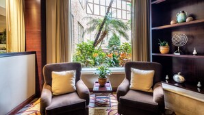 Una habitación con dos sillones, una mesita con una planta y una estantería con objetos decorativos.