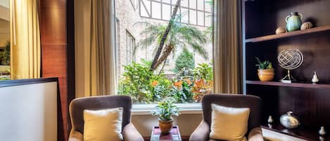 A room with two armchairs, a small table with a plant, and a bookshelf with decorative items.