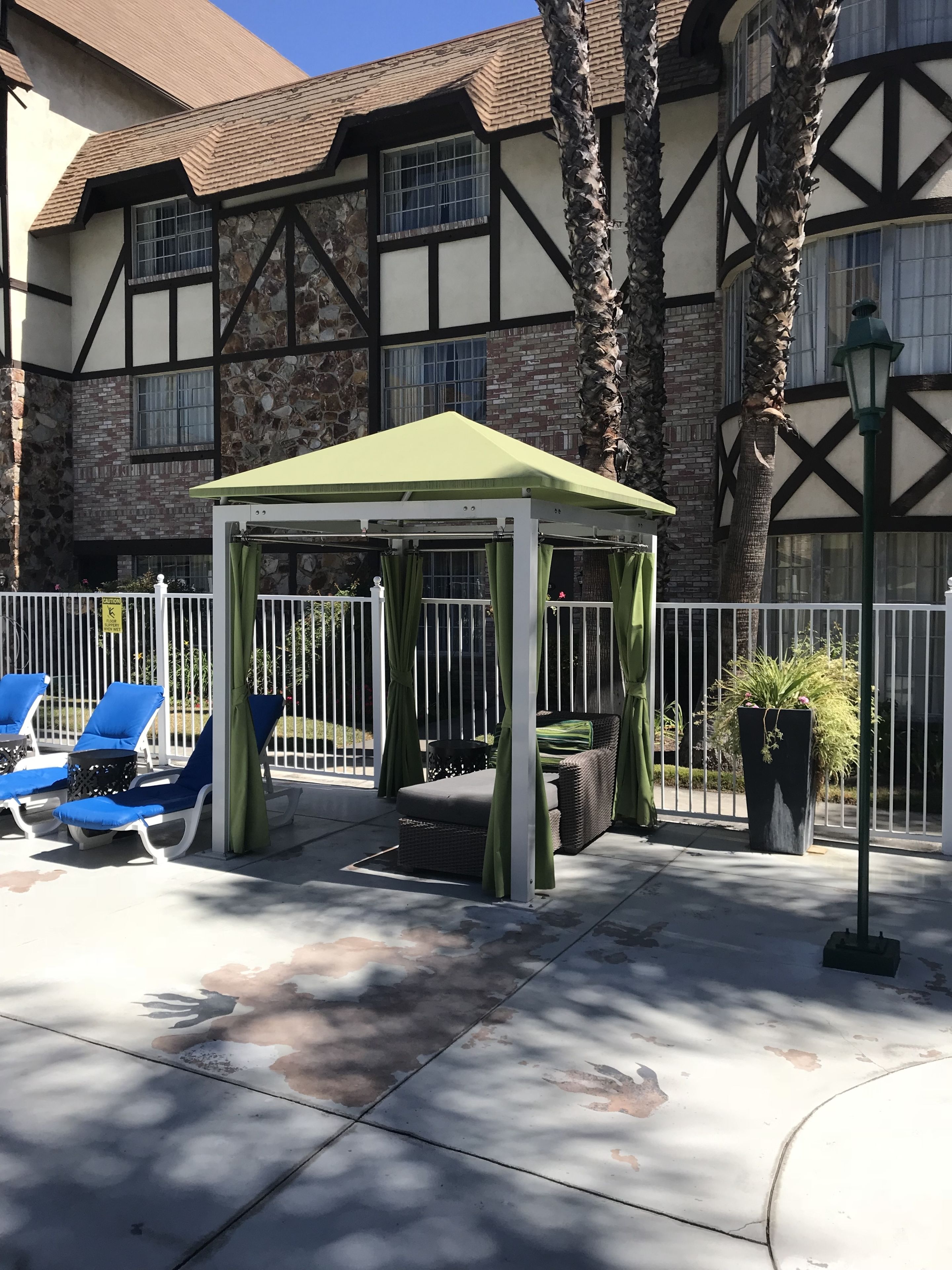 A gazebo with a green roof, surrounded by white railings, and blue lounge chairs.