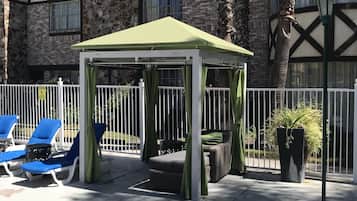 A gazebo with a green roof, surrounded by white railings, and blue lounge chairs.