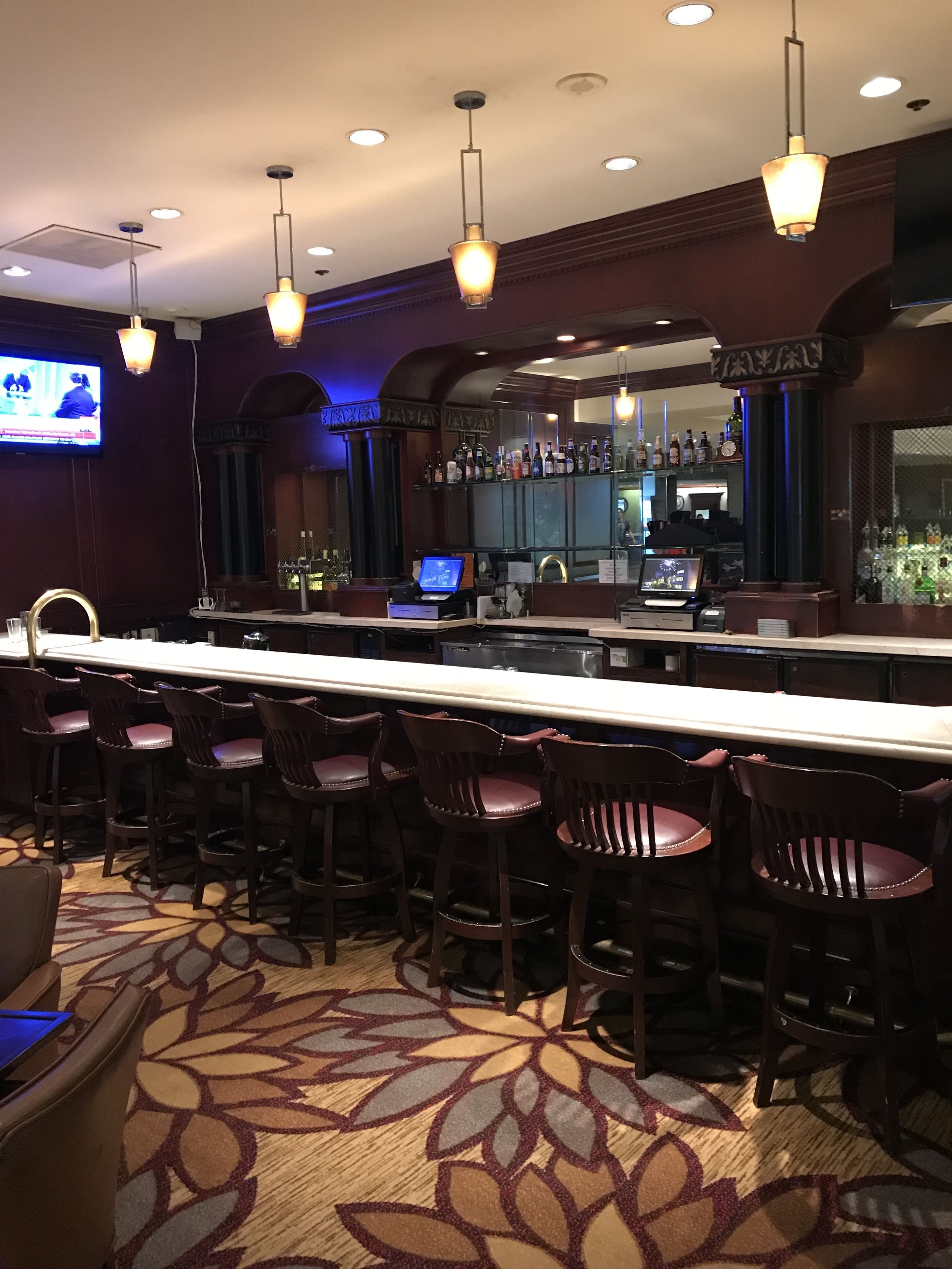A bar area with a long counter, multiple bar stools, and overhead lighting.