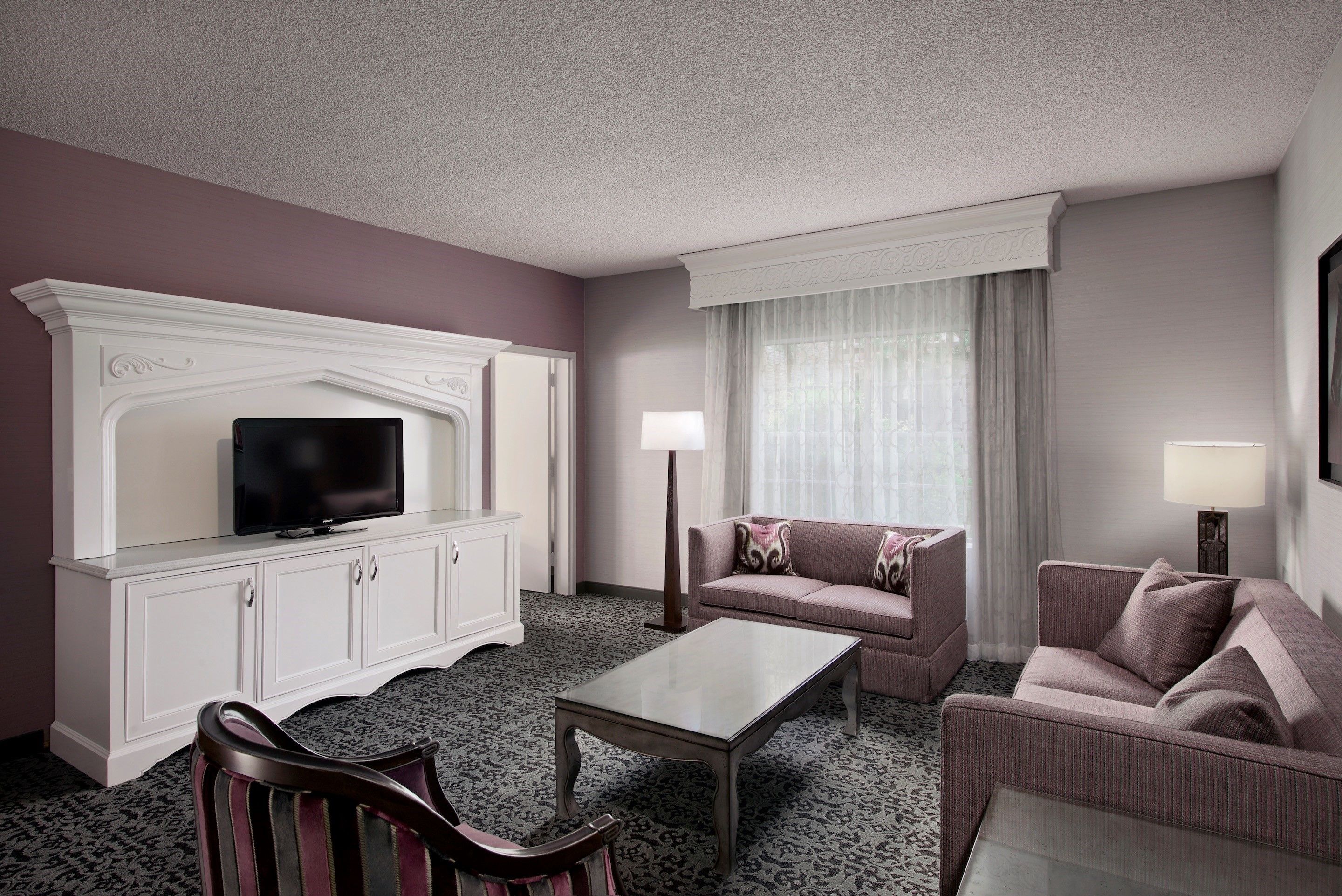 A hotel room with a television on a white cabinet, a sofa, a chair, and a coffee table.
