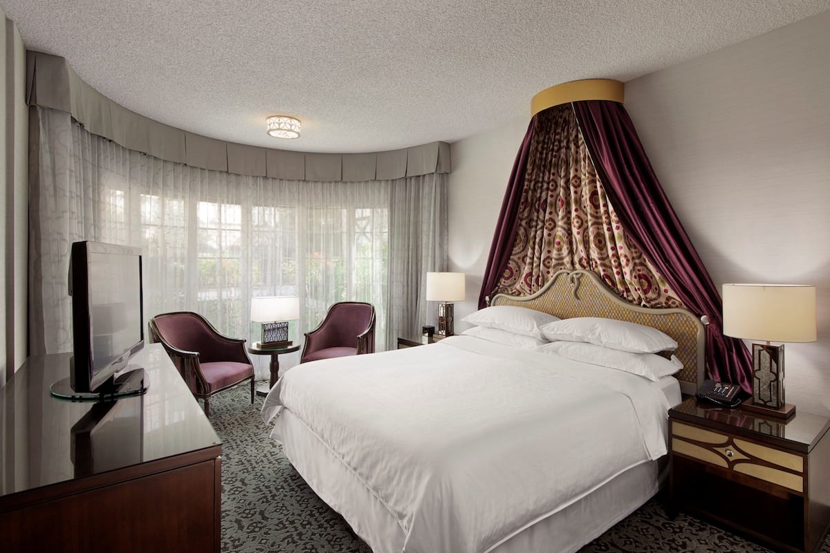 A hotel room with a large bed, a TV, a desk, and a chair.