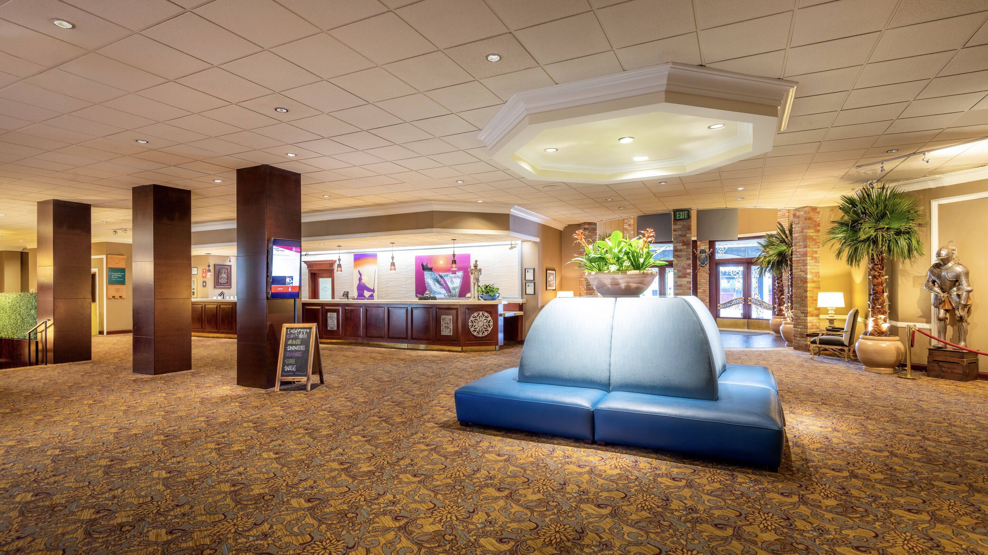 A lobby with a reception desk, a blue seating area, and a large plant.